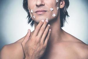 Really bad shave. Close-up of frustrated young shirtless man touching his face and expressing negativity while standing against grey background photo