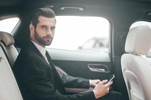 pensando en nuevas posibilidades. un joven hombre de negocios confiado configurando su teléfono inteligente y mirando la cámara mientras está sentado en el auto foto