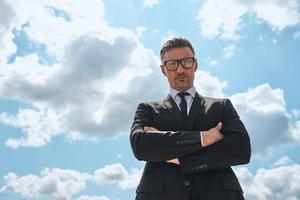 Low angle view of confident mature man in full suit keeping arms crossed photo