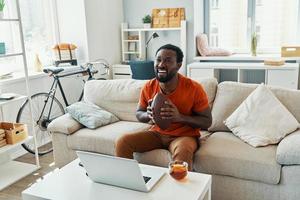 Happy young African man cheering and smiling while watching sport match at home photo