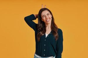 Playful young woman in casual clothing making a face while standing against yellow background photo