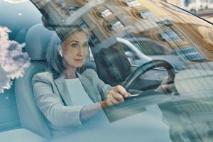 Mature beautiful woman in smart casual wear looking ahead while driving car photo