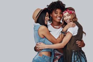 Three attractive stylish young women embracing and laughing while standing against grey background photo