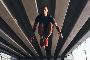 Fantastic gymnastics. Handsome young African man in sports clothing jumping and smiling while exercising outdoors photo