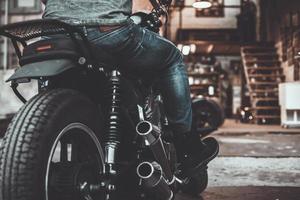 On the way to his garage. Close-up rear view of man sitting on his bike with motorcycle garage in the background photo