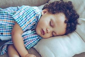 Sweet dreams. Little African baby boy sleeping while lying on couch at home photo