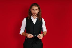 Charming young man in elegant clothing looking at camera while standing against red background photo