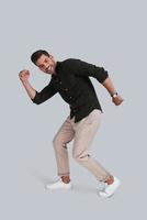 Going crazy. Full length of playful young man dancing and smiling while standing against grey background photo