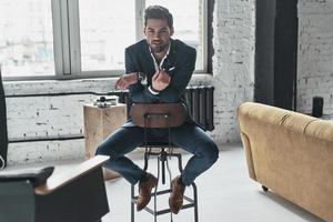 Charming man. Handsome young man in full suit looking at camera and smiling while sitting on the stool photo