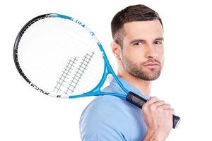 Ready to play. Confident young man holding tennis racket and looking at camera while standing against white background photo