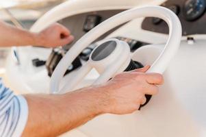 All the ways in a hand. Close-up of young man holding hand on steering wheel while driving yacht photo