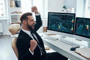 Happy young man in shirt and tie cheering and gesturing while working in the office photo