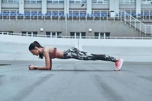 Her body is perfect. Beautiful young woman in sports clothing keeping plank position while exercising outdoors photo