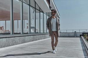 Businessman on the go.  Full length of confident young and handsome man keeping hands in pockets and looking away while walking outdoors photo