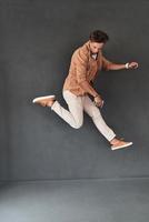 Feeling free to do anything. Full length of handsome young man listening music while jumping against grey background photo