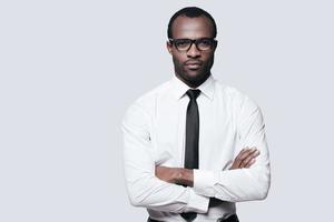 Young and successful. Handsome African man looking at camera and keeping arms crossed while standing against grey background photo