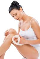 Making her legs perfect. Beautiful young woman massaging her legs while sitting against white background photo