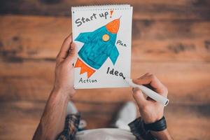 Planning his own start up. Top view of man drawing in note pad while standing on the wooden floor photo