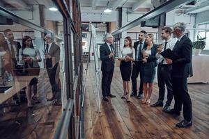 longitud total de un hombre de negocios moderno que realiza una presentación mientras se reúne el personal en el pasillo de la oficina foto