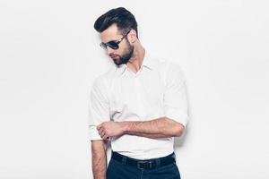 Used to look perfect. Handsome young man in white shirt adjusting his sleeve while standing against white background photo