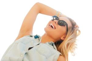 Enjoying sunshine. Low angle view of cheerful young woman holding hand in hair and smiling while standing outdoors photo