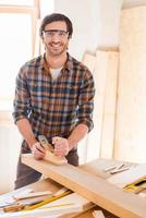 Skilled carpenter. Cheerful young male carpenter working with wood in his workshop photo