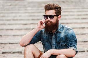 Staying in touch. Confident young bearded man talking on the mobile phone while sitting outdoors photo