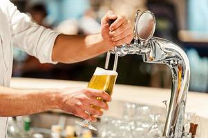 sirviendo cerveza fresca. primer plano de un joven camarero sirviendo cerveza mientras está de pie en el mostrador del bar foto