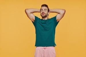 Relaxed young man in casual clothing holding head in hands while standing against yellow background photo