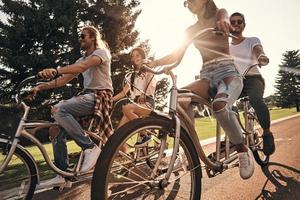 cálido sol y una gran compañía. grupo de jóvenes felices con ropa informal sonriendo mientras andan en bicicleta juntos al aire libre foto