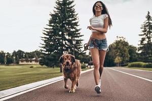 Full length of beautiful young woman running with her dog through the park and smiling while spending time outdoors photo