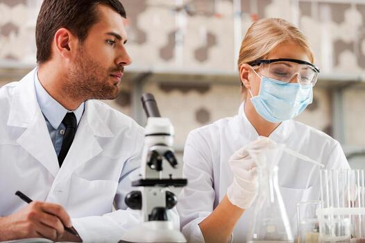 Researches in science laboratory. Low angle view of two young scientists making experiments while sitting in the laboratory photo