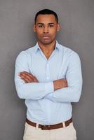 Confident and handsome. Confident young African man keeping arms crossed and looking at camera while standing against grey background photo