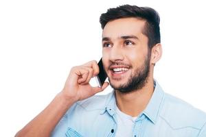 Good talk with friend. Handsome young Indian man talking on the mobile phone and smiling while standing against white background photo