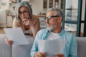 Busy senior couple in casual clothing taking care of their finances while bonding together at home photo