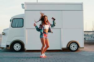 Totally carefree. Full length of attractive young woman in sports clothing dancing and smiling while standing against food truck outdoors photo