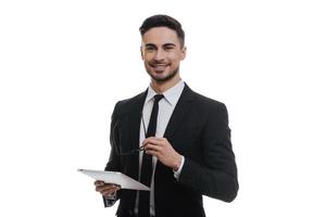 He always right. Handsome young man in full suit holding digital tablet and smiling while standing against white background photo