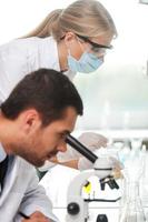 Scientists at work. Side view of male scientist using microscope while his female colleague making experiment in the background photo