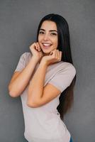 Feeling excited. Beautiful young woman holding hands near face and looking excited while standing against grey background photo