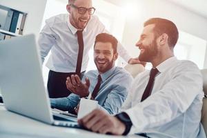 Happy to work together. Group of young modern men in formalwear working using computers and smiling while sitting in the office photo