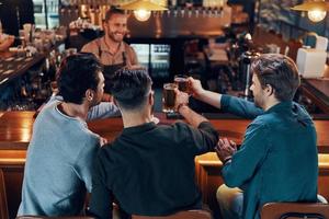 jóvenes despreocupados con ropa informal bebiendo cerveza mientras se sientan juntos en el pub foto