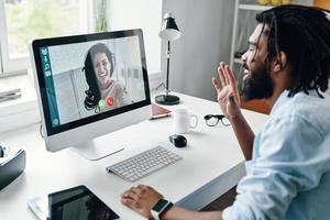 joven africano confiado en camisa hablando con una mujer sonriente usando una computadora mientras se sienta en el interior foto