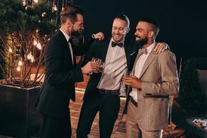 Three handsome men in suits drinking whiskey and communicating while spending time on party photo