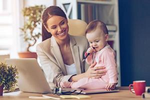 Helping to mommy. Little baby girl chewing pen while sitting on office desk with her mother in office photo