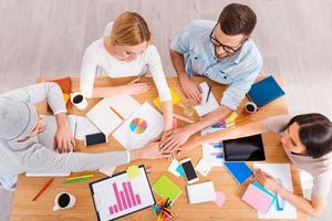 The best creative team. Top view of group of business people in smart casual wear holding hands together while sitting at the wooden desk photo