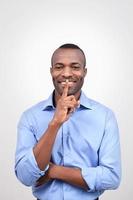 Keep silence. Handsome African man holding finger on mouth and smiling while isolated on grey photo