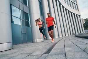 Full length of confident fit couple in sports clothing enjoying morning jogging while practicing outdoors on the city street photo