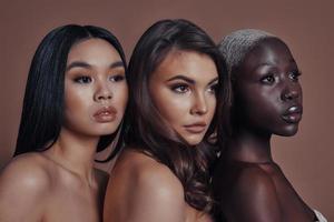 Glowing with natural beauty. Three attractive young women looking away while standing against brown background photo