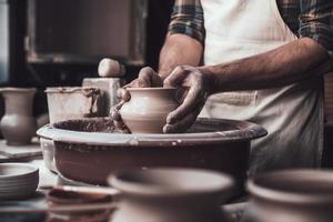 Creative work. Close-up of man making ceramic pot on the pottery wheel photo