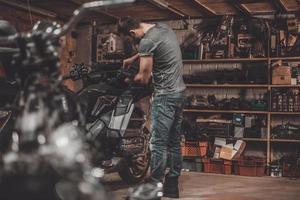 Spending time with bikes. Confident young man repairing motorcycle in repair shop photo